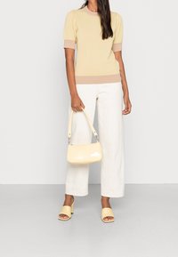 Sweter z żółtą kratą, krótkie rękawy, beżowe akcenty; białe szerokie spodnie; błyszcząca żółta torebka; żółte sandały na obcasie.