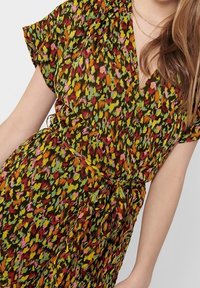 Kwiatowa sukienka kopertowa wykonana z materiału z wielokolorowym wzorem w odcieniach zieleni, różu, pomarańczy i żółci; zawiera detal w postaci wiązania w talii.