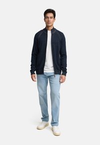 Marineblauwe gebreide trui met een ritssluiting aan de voorkant, ribbelkraag en manchetten, gecombineerd met lichtblauwe jeans en witte sneakers. Eenvoudig en textuurrijk ontwerp.
