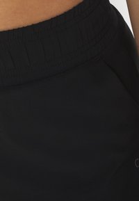 Pantalones cortos deportivos negros con cintura elástica y textura suave, con un pequeño detalle de logo en el costado.