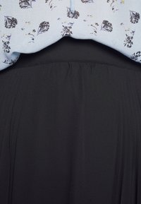 Blusa floral azul clara acima de uma saia preta plissada. A blusa apresenta pequenos padrões escuros, enquanto a saia tem uma textura suave e fluida.
