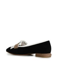 Scarpa piatta in suede nera con punta affilata, caratterizzata da un fiocco in suede marrone a contrasto e dettagli bianchi sul bordo. Tacco basso e impilato.