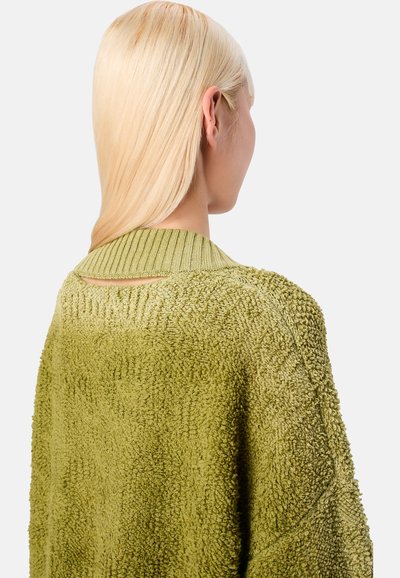 Vihreä, teksturoitu vaate, jossa on ribbireunus ja avoin yksityiskohta selässä, nähtynä takaa suoria vaaleita hiuksia näkyvissä.