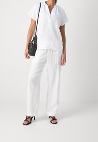 Haut à manches courtes en lin blanc avec un col droit, associé à un pantalon ample en lin blanc. Sac à bandoulière noir et talons ouverts noirs complètent le look.