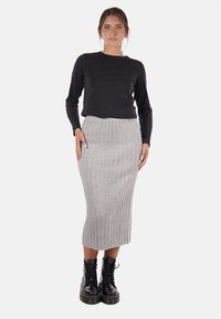 Maglietta nera a maniche lunghe, gonna midi in maglia grigia a coste, e stivali neri chunky con lacci, con una silhouette aderente e tessuto testurizzato.