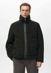 Giacca in pile nera con colletto alto, zip frontale e due grandi tasche. Caratterizzata da una morbida texture e un design dalla vestibilità comoda.