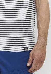 Camisa de manga corta a rayas con rayas horizontales en azul marino y blanco. Incluye una etiqueta negra con "FQ1924 ORIGINAL" cerca del dobladillo.
