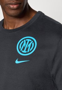 Sort bomulds T-shirt med et stort turkist logo med cirkulært design og tekst, samt et mindre turkist Nike logo foran.
