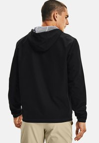 Giacca a vento nera con cappuccio, caratterizzata da una fodera in rete, polsini regolabili e una superficie liscia.