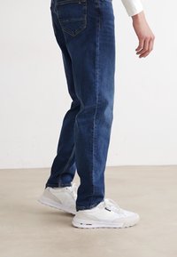 Mørkeblå denimjeans med rett ben, parret med hvite sneakers med teksturdesign og subtile grå detaljer.