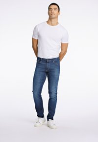 Blaue Slim-Fit-Jeans kombiniert mit einem weißen, figurbetonten T-Shirt und weißen Sneakers, mit standardmäßigen Nähten und einer glatten Textur.