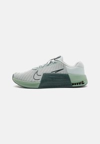 Világosszürke sportcipő, hálós felsőrésszel, zöld akcentusokkal és texturált talppal. A cipő oldalán egy jellegzetes swoosh logó található.