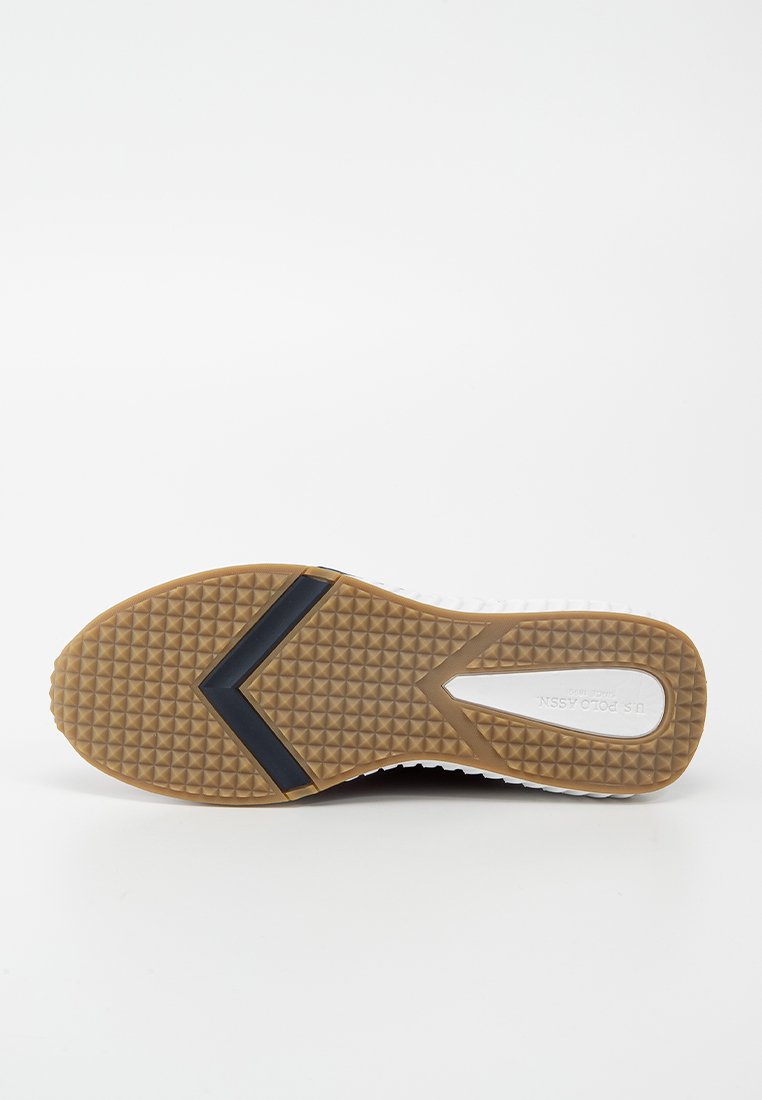 Semelle de sneaker blanche avec un fond en caoutchouc gomme texturé, featuring un accent noir triangulaire et une semelle intermédiaire blanche lisse.