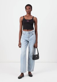 Top corto nero con logo rosa, jeans a gamba larga azzurri, ballerine nere e borsa nera piccola con dettaglio di logo colorato.