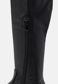 Botte haute jusqu'au genou en cuir noir avec une texture lisse, fermeture éclair latérale et coutures renforcées le long de la couture pour la durabilité et le style.