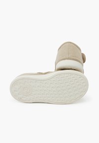 Beige plátěná obuv s bílou gumovou podrážkou. Obsahuje strukturovaný svršek a zaoblenou špičku. Zapínání zahrnuje pásek. Nenápadné logo na podrážce.
