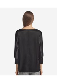 Schwarze Satinbluse mit rundem Ausschnitt, Dreiviertelärmeln und lockerer Passform. Glatte Textur mit einem subtilen Glanz, ohne Muster oder Akzente.