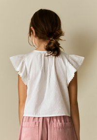 Balta kokvilnas krekls ar volānu piedurknēm, rotāts ar teksturētām rakstām. Kombinēts ar maigām rozā kordurjū šortiem ar lielām kabatām.