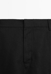 Zwarte linnen broek heeft een rechte snit, zijzakken en een verborgen tailleband. De stof heeft een licht gestructureerde afwerking.