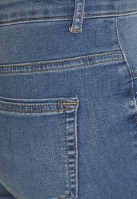 Bolso de jeans de denim, lavagem azul média, com costura castanha clara; apresenta uma textura subtil e um design clássico de cinco bolsos.