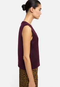 Bordowy bezrękawnik o luźnym kroju i szerokich armiach, zestawiony z brązowymi spodniami w cętki. Miękka tekstura i prosty dekolt.