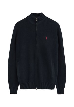 Jersey negro de punto con cremallera completa, cuello alto, bolsillos laterales, puños y bajo acanalados, y un pequeño logo rojo en el pecho izquierdo.