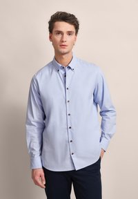 Hellblaues Button-up-Hemd mit langen Ärmeln, das braune Knöpfe und einen Kragen hat. Hergestellt aus glattem Stoff mit lockerer Passform.