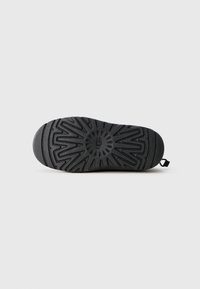 Black rubber sole of a shoe with geometric tread pattern and "UGG" logo embossed in the center on a plain white background.
