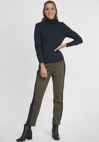 Maglione dolcevita blu navy, con orlo a coste, abbinato a pantaloni verde oliva con strisce laterali blu navy e stivali neri alla caviglia.
