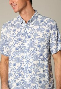 Korte mouw shirt van lichte stof, met een blauw tropisch palmbladpatroon op een witte achtergrond, met een knoopsluiting op de kraag en een relaxte pasvorm.