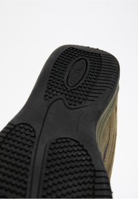 Zwarte rubberen zool met gestructureerde grippatronen, inclusief verhoogde stippen en groeven, bevestigd aan een tan suède bovenwerk.