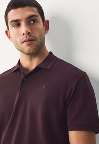 Vyriški bordo spalvos polo marškinėliai iš lygaus, tekstūruoto audinio. Su klasikiniu apykakle, dviem sagačiais ir mažuoju išsiuvinėtu logotipu ant krūtinės.