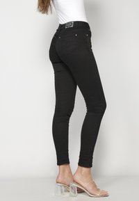 Black denim skinny jeans with a high waistband, subtle embroidery on the back pocket, and silver-tone hardware accents.