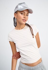 Balta ir smėlinė dryžuota prigludusi marškinėliai su trumpomis rankovėmis, su iškilniu "Nike" logotipu ant krūtinės; derinama su pilkais sportiniais kelnais.