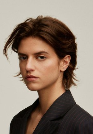 Retrato de una persona con cabello corto castaño, que lleva una chaqueta de traje oscura con finas rayas. Accesorios mínimos, textura facial sutil.