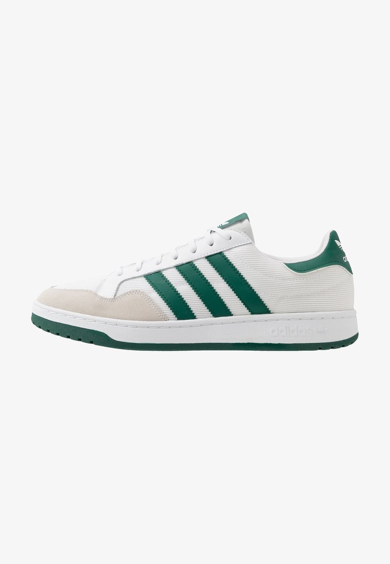 White sneaker with green accents, featuring three green stripes, textured fabric upper, suede toe cap, and a rubber sole.