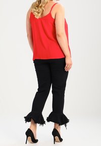 Haut sans manches rouge associé à un jean noir avec des ourlets volants et effilochés, et des chaussures à talons hauts noires.