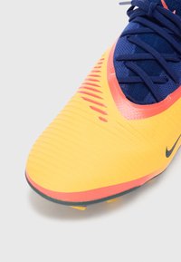 Soccer shoe with a bright yellow upper, textured surface, navy blue tongue, red accents, and black Nike logo on the side.