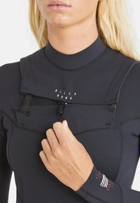 Schwarzer Neoprenanzug mit hohem Kragen und Reißverschlussdetails an der Vorderseite. Verfügt über flache Nähte und Logodetails auf der Brust und an den Manschetten.
