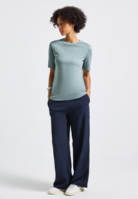 Světle modrý top s krátkým rukávem, tmavě modré plisované široké kalhoty a bílé tenisky. Oblečení má uvolněný střih a jemnou strukturu.