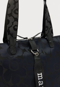 Τσάντα σε μπλε ναυτικό χρώμα με μαύρο λουλουδάτο μοτίβο, υφασμάτινη υφή, διπλά ανθεκτικά λουριά και κλείσιμο με φερμουάρ που διαθέτει μεταλλικά εξαρτήματα και λεπτομέρεια με λογότυπο.