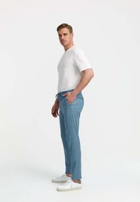 Light blue trousers made of soft fabric with a drawstring waistband, paired with a white T-shirt and white sneakers. Slim fit design.