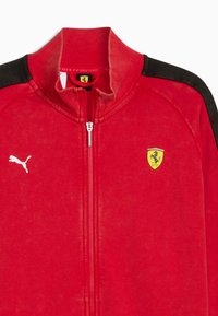 Rød zip-up jakke med sorte skulderdetaljer, ribbet krave og et hvidt Puma-logo. Har et Ferrari-skjold badge på brystområdet.