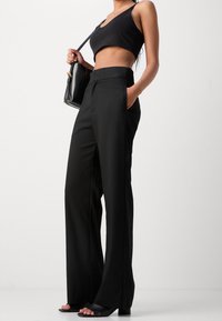 Pantalones anchos negros a medida con textura suave, cintura alta, bolsillos laterales, combinados con un top negro corto y sandalias negras de tacón sencillas.