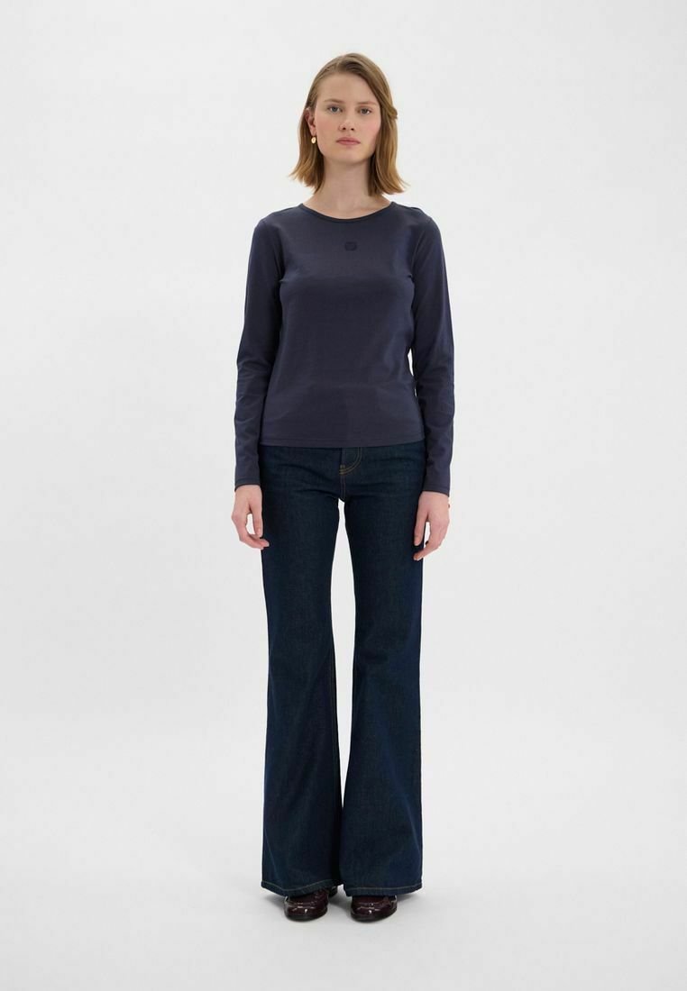 Chemise à manches longues navy en tissu lisse ; col rond. Associée à un jean en denim foncé évasé, avec un design de poche classique.
