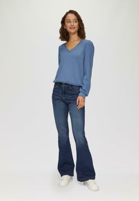 Lichte blauwe langemouw v-hals top, gecombineerd met donkerblauwe flared jeans en witte sneakers, met een relaxed fit en een zachte textuur.