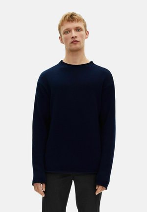 Donker marineblauwe gebreide trui met een ronde halslijn, verlaagde schouders en lange mouwen. De stof heeft een gestructureerde, geribbelde uitstraling. Zwarte broek.