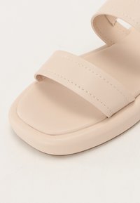 Nude open-toe sandal featuring two wide straps, smooth faux leather material, flat sole, and subtle stitching details.