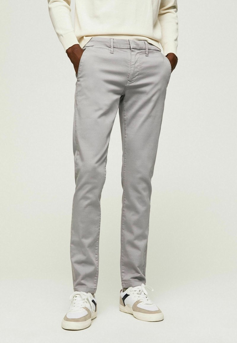 Lysegrå chinos med en slank pasform, der har en glat bomuldsstruktur og standardlommer. Kombineret med hvide og beige sneakers.