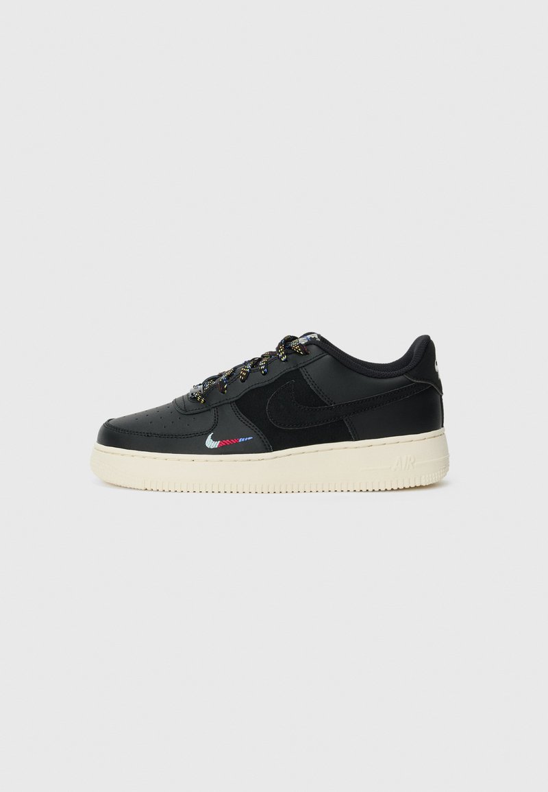 Baskets basses noires avec semelle crème, logo Nike multicolore près de l'orteil et lacets noirs avec accents jaunes, montrées de profil.